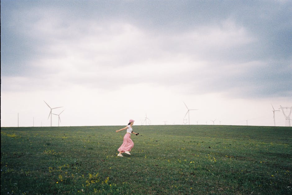 A woman runs joyfully in a spacious field with wind turbines on a cloudy day in Inner Mongolia.