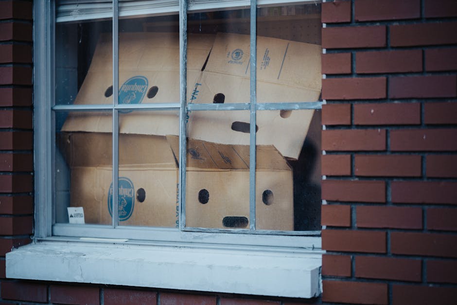 View of stacked cardboard boxes through a window with a red brick facade, illustrating urban storage solutions.