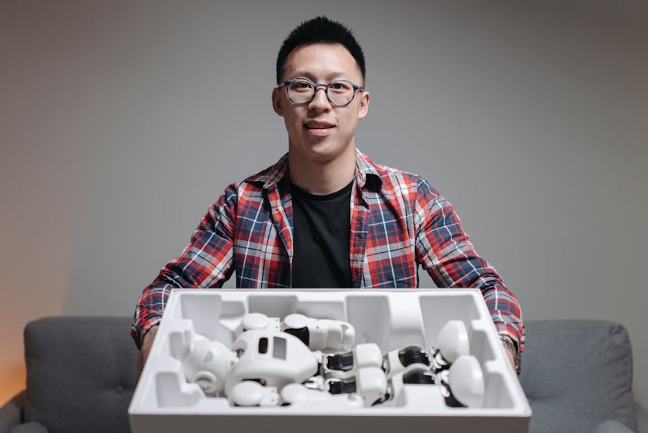 Asian man holding a box with robot components, showcasing technology and innovation indoors.