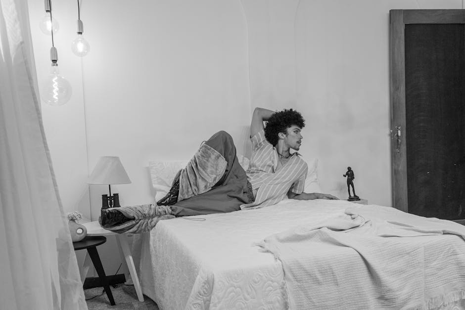Black and white photo of a man lounging in a stylish and serene bedroom setting.
