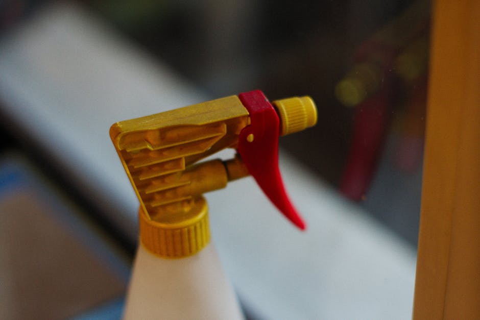 Detailed view of a yellow and red spray bottle nozzle in focus.