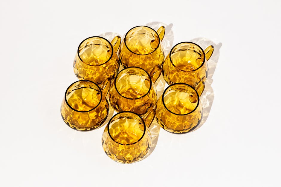 Abstract arrangement of amber glass mugs on a white background with reflective shadows.