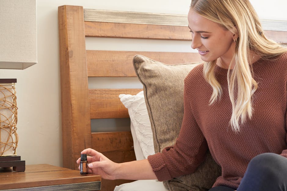 Woman in red sweater placing a bottle of essential oil on a bedside table. Indoor setting.