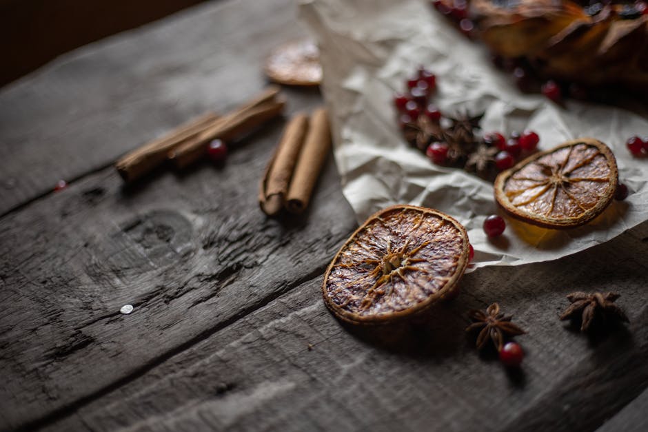 A rustic still life of dried orange slices, cinnamon sticks, and star anise on a wooden table.