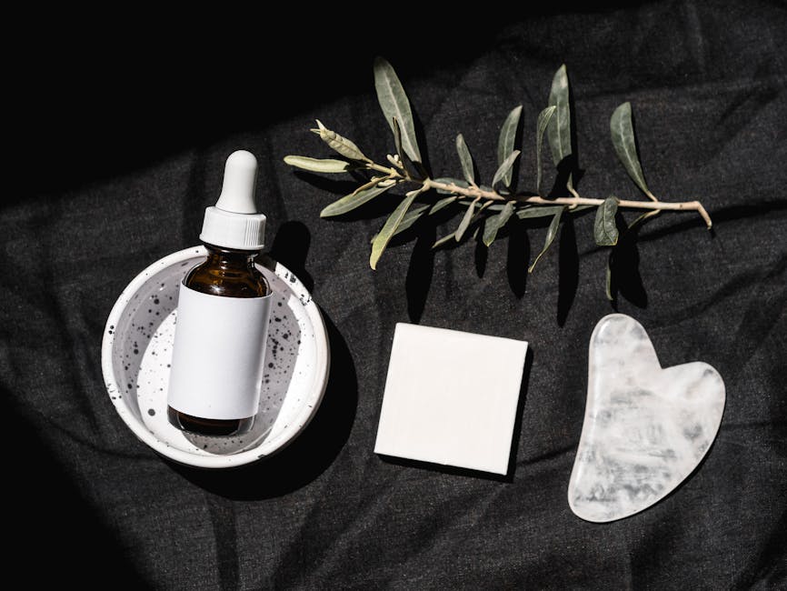 Elegant beauty product arrangement featuring a serum dropper bottle and gua sha on a black background.