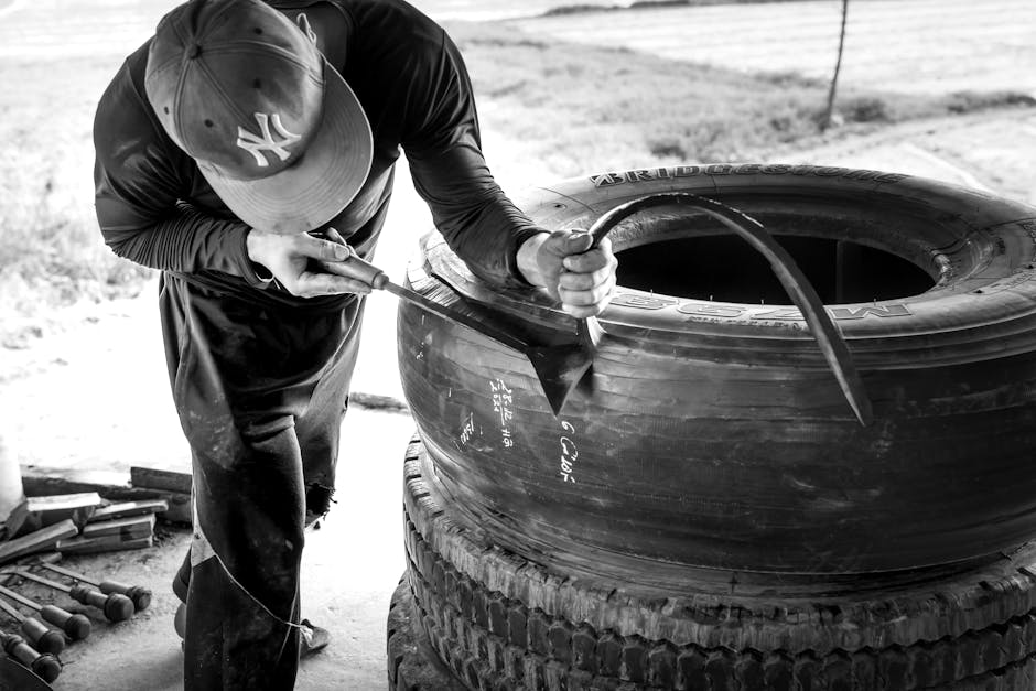 A detailed black and white photo of a man repairing a large industrial tire outdoors.