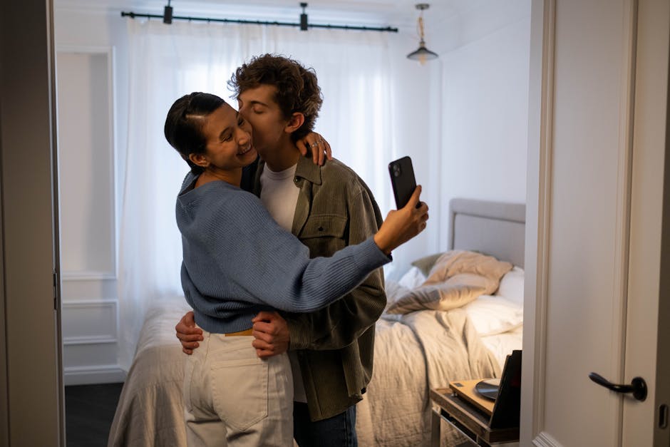 A joyful couple embracing and taking a selfie in a cozy bedroom setting.