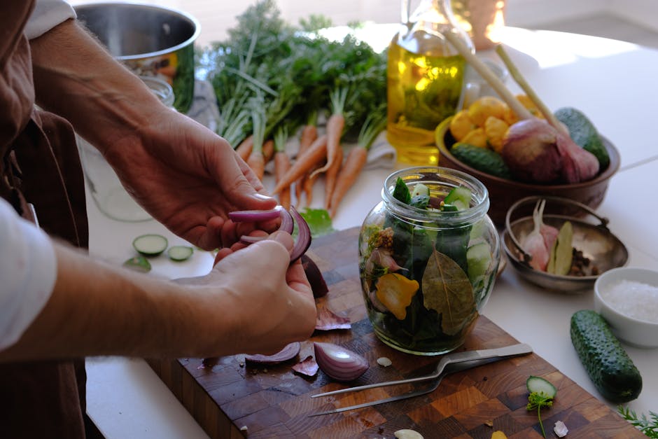 Close-up of hands preparing pickled vegetables in a jar with fresh carrots and cucumbers.