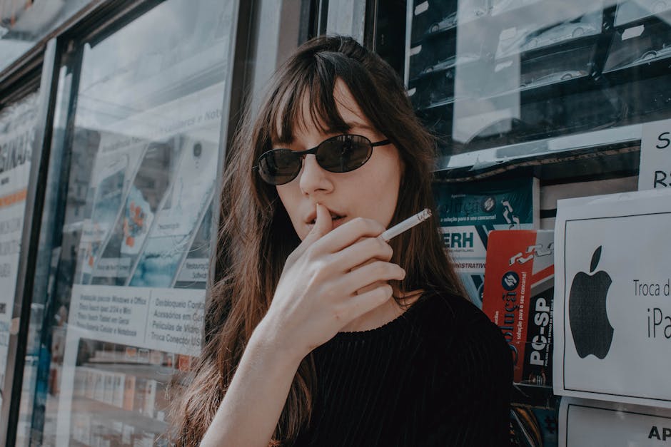 Stylish woman smoking outside a storefront, wearing sunglasses, conveying a moody urban vibe.