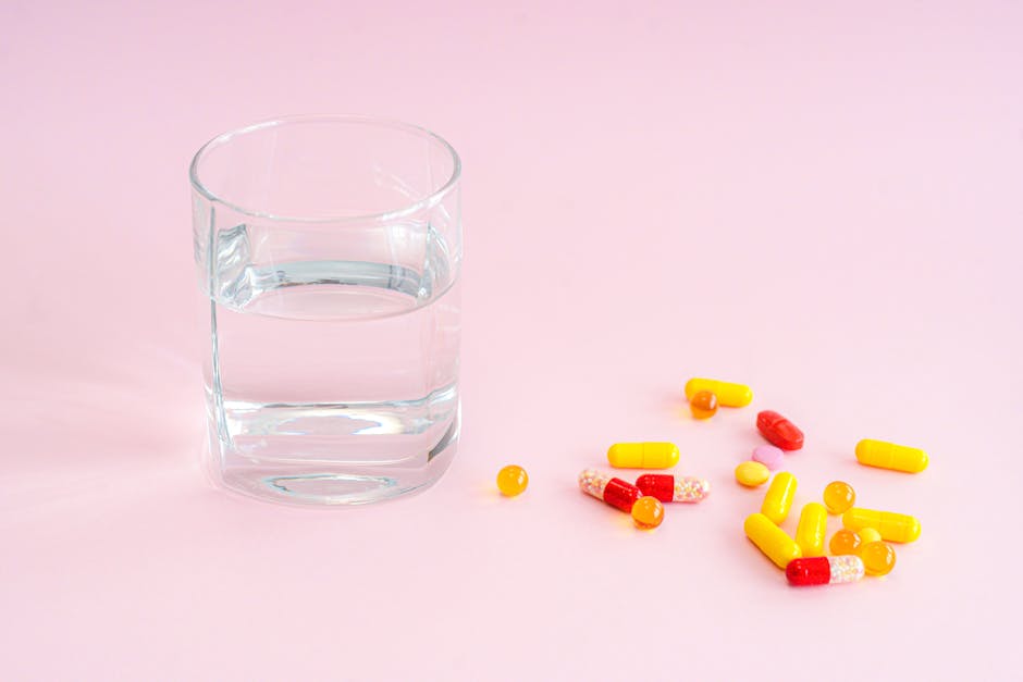 A glass of water and variety of pills on a pink background, symbolizing medication.