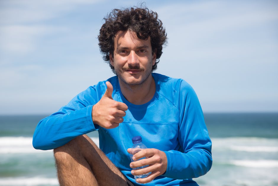 Smiling man in blue long sleeves with curly hair gives a thumbs up at the beach in Portugal.