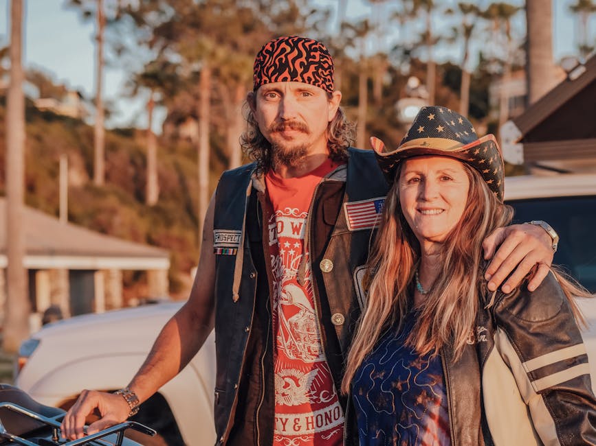 A middle-aged couple wearing leather and cowboy attire, embracing outdoors at sunset.