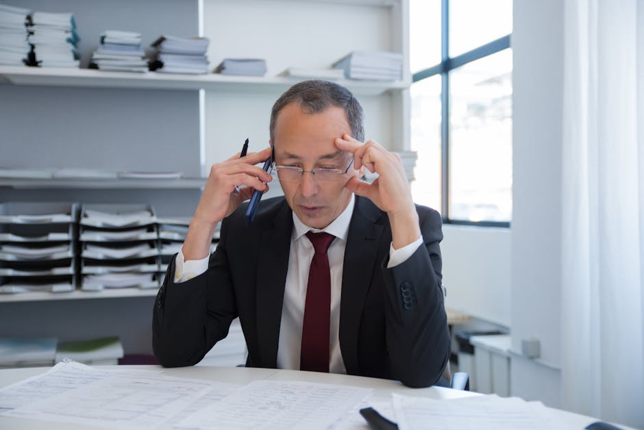 Businessman in a black suit stressed over documents in a bright office setting.