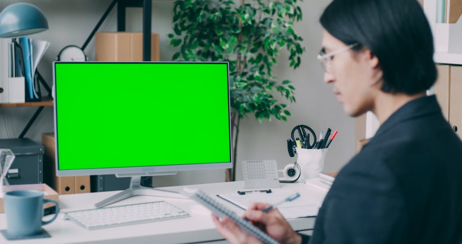 Business professional working in a modern office with a green screen computer setup.