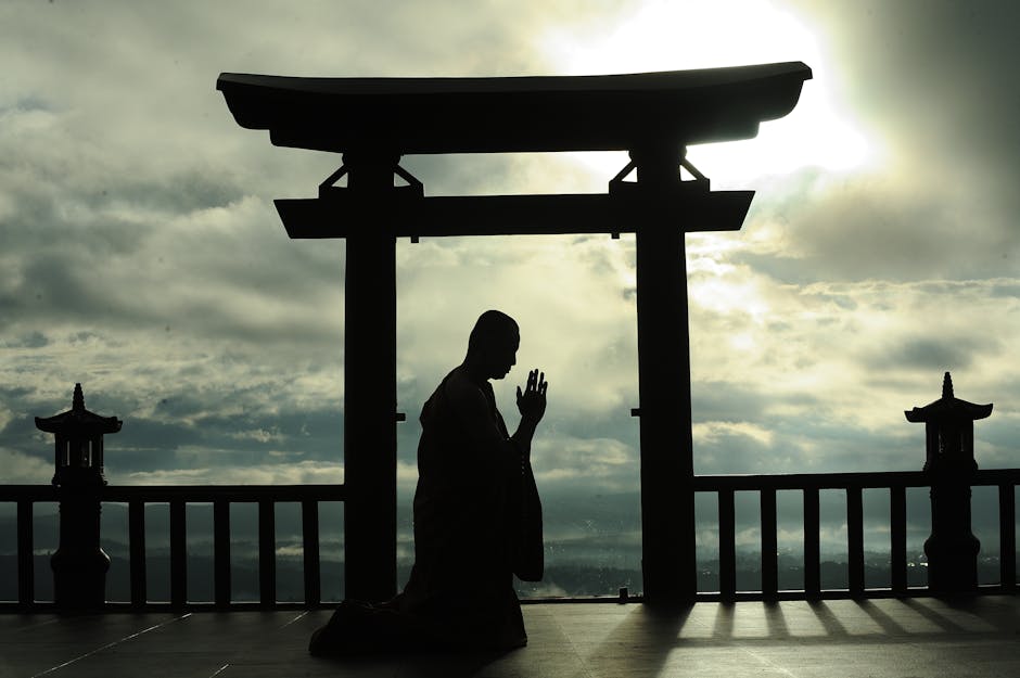Silhouette of a man meditating in prayer under a Torii gate at sunrise, symbolizing peace and spirituality.