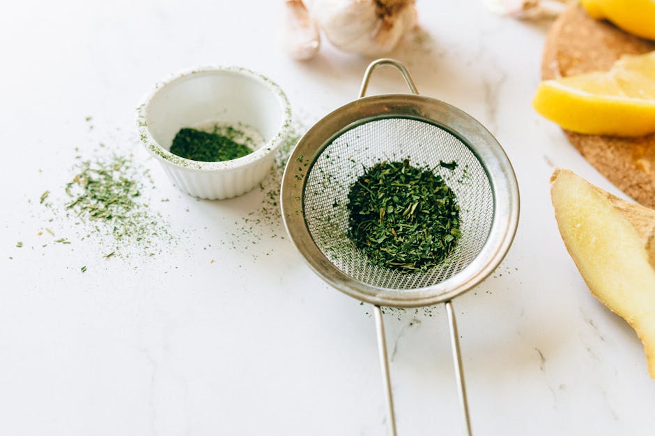 Close-up of fresh herbs in a strainer with garlic and ginger on a marble counter, ideal for natural remedy themes.