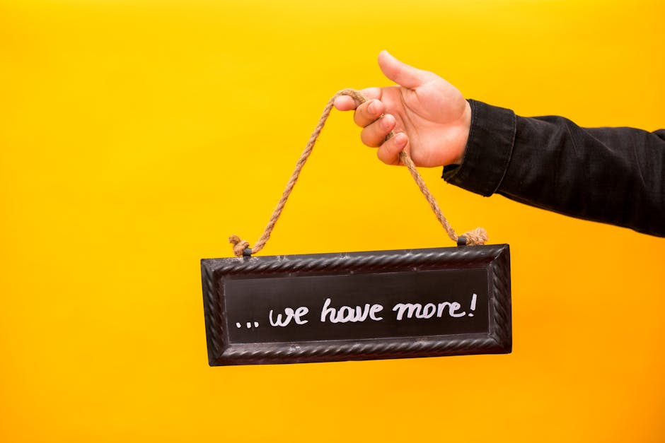 A hand holding a sign that reads 'we have more' against a yellow background.