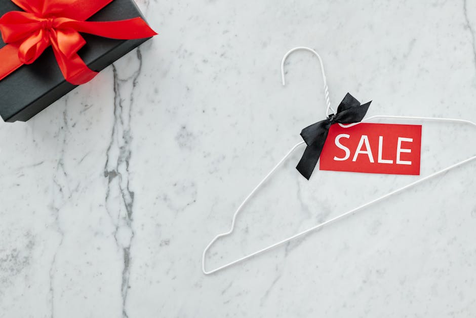 Flat lay of a sale tag on a hanger and gift box on marble, perfect for holiday promotions.