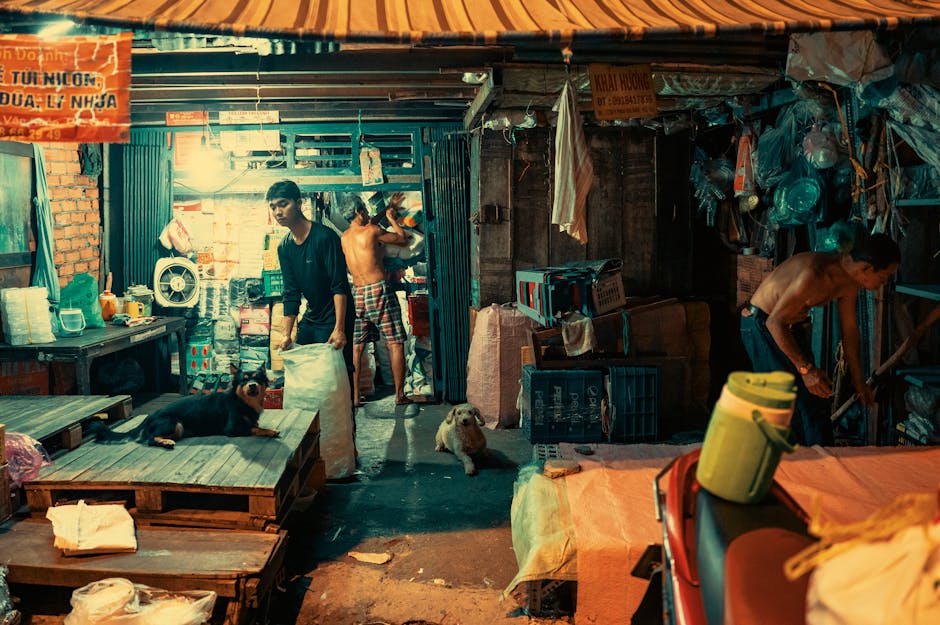 Vibrant night market scene with people working and dogs resting at a stall.