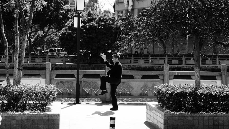 Serene black and white photo of a man practicing Tai Chi in an urban park in China.