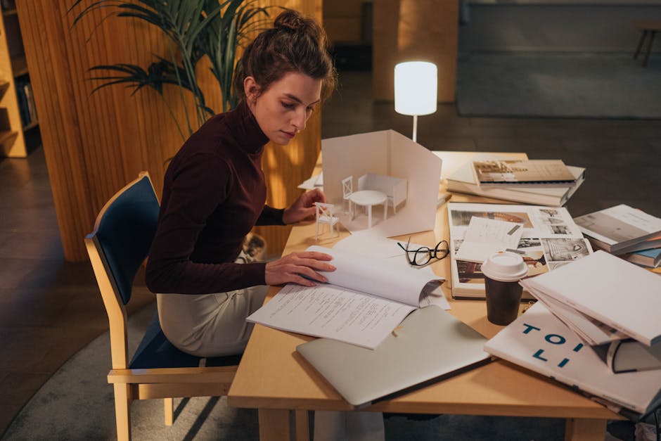 A young woman concentrating on architecture designs at a desk, surrounded by books and a laptop.
